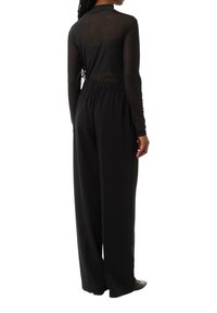 Czarny przezroczysty top z długim rękawem w połączeniu z szerokimi spodniami. Strój ma zg gathered elastyczny pas i gładką fakturę.