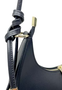 Černá kožená kabelka s hladkým povrchem, se zkrouceným popruhem, zlatými kovovými detaily a viditelným zipem.