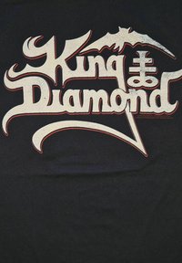 Černé tričko s velkým, stylizovaným bílým a červeným nápisem "King Diamond" s propracovaným písmem a netopýřími doplňky.