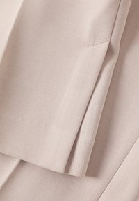 Tessuto rosa chiaro con una superficie liscia, caratterizzato da bordi ripiegati e sottili dettagli di cucitura, creando un aspetto pulito e strutturato.
