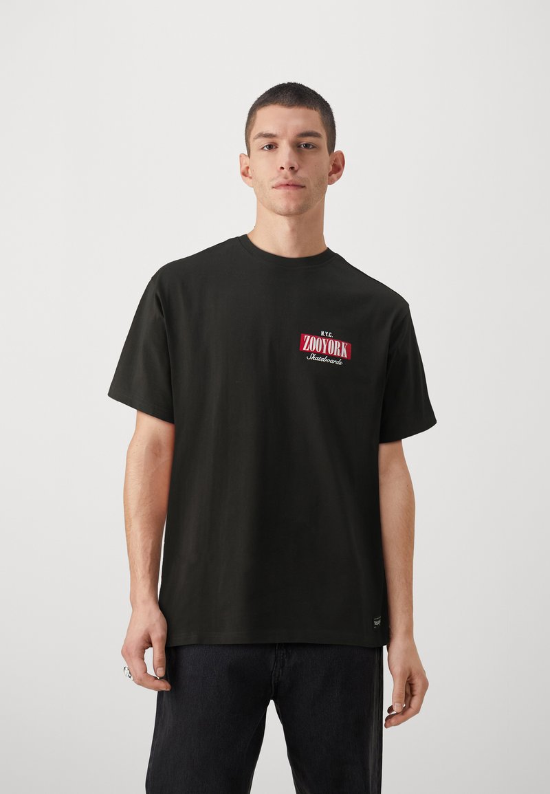 Sort bomulds T-shirt med korte ærmer, rund hals, med et rødt og hvidt "ZOYORK" logo på venstre bryst. Tekstureret stof, afslappet fit.