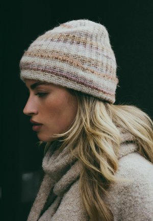 Knitted wool beanie with a cream base and multicolored stripes in brown and pink. The hat has a rounded crown and ribbed texture.