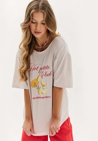 Beige oversized tričko s grafikou "Hot Potato Club", na které jsou žluté brambory a bylinky. Měkká látka, uvolněný střih, krátké rukávy.