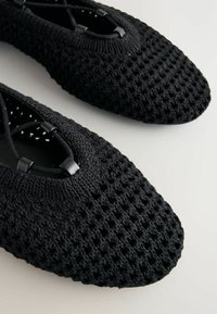 Svarta stickade lägenheter med en texturerad yta, med ett öppet vävningsmönster och en rund tådesign. Justerbara svarta snörakcenter ingår.