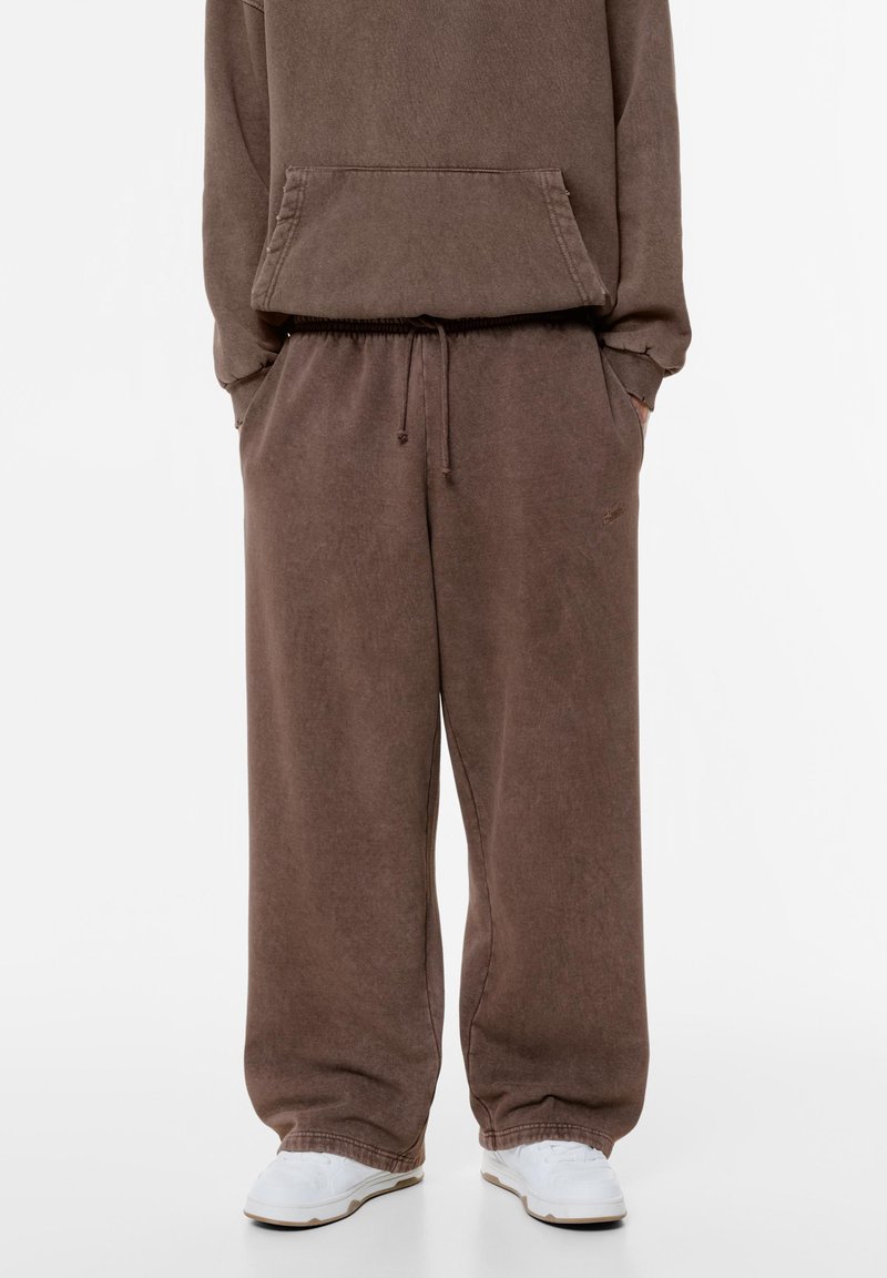 Lichte, comfortabele sweatpants in bruin met een elastische tailleband en zijzakken, gemaakt van zachte stof, gecombineerd met witte sneakers.