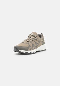 Scarpa sportiva beige con tomaia in rete, accenti grigi, punta arrotondata, ampio intersuola bianca e suola nera robusta. Presenta lacci e logo.