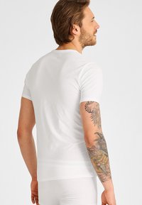 Hvit t-skjorte med korte ermer, tettsittende stil, glatt bomullsstoff. Har rund hals og enkel design, brukt sammen med hvite undertøy.