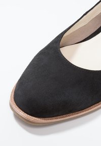 Chaussure plate en suédine noire avec un bout lisse et arrondi, et une semelle en caoutchouc beige avec des détails de couture le long du bord.