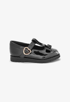 Chaussure pour enfants de style Mary Jane en cuir verni noir avec boucle en forme de cœur dorée et petit nœud sur le bout arrondi, semelle plate.