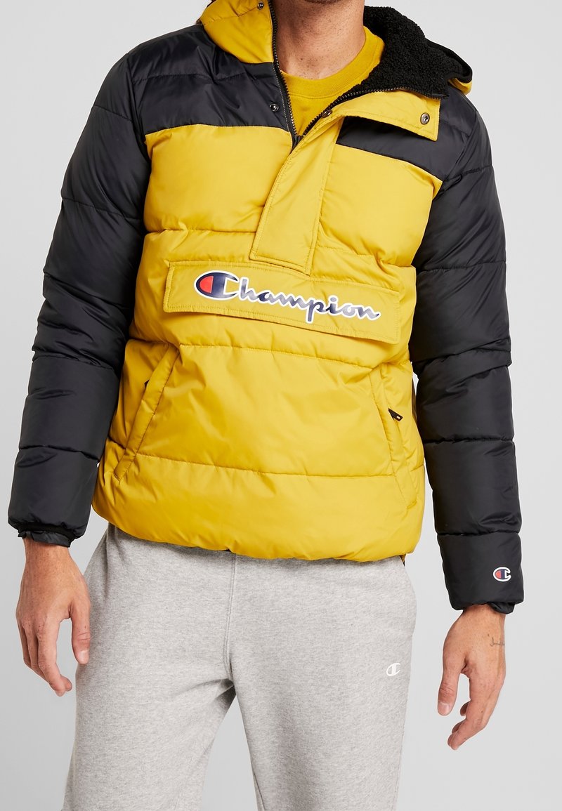 Gul och svart pufferjacka med halvdragkedja fram, utrustad med en logotyp-etikett, sidofickor och en fleecefodrad krage. Strukturerad, quiltad design.