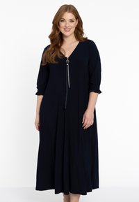 Navyblaues Midikleid mit V-Ausschnitt, goldenen Reißverschlussdetails und lockeren Ärmeln. Hergestellt aus weichem Stoff mit fließender Silhouette.