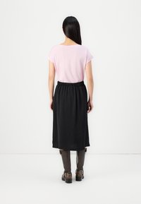 Rosa kortärmad topp i kombination med en svart knä-lång kjol. Kjolen har elastisk midja med en texturerad finish. Bruna knähöga stövlar.