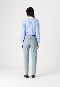 Sininen raidallinen paita, jossa valkoinen kaulus ja takana logotähti, yhdistetty vaaleansinisiin suoriin farkkuihin ja mustiin kenkiin.