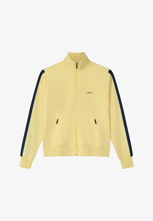 Jachetă galbenă cu fermoar, cu dungi negre pe mâneci, două buzunare frontale cu fermoar și un mic logo brodat pe piept.