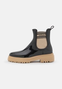 Botas Chelsea de charol negro con un panel lateral elástico beige, suela gruesa de goma marrón claro y una lengüeta para facilitar su uso.