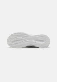 Semelle de chaussure blanche avec des rainures texturées et une indentation centrale en forme d’onde, présentée sur un fond clair uni.