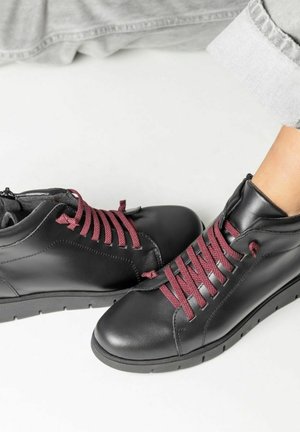 Botas de tobillo de cuero negro con cordones burdeos, punta redondeada y suela texturizada, con un detalle de cremallera para facilitar su uso.