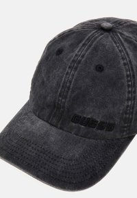 Gorra de béisbol de algodón negra con visera curvada, tejido texturizado y logotipo "GUESS" en relieve en la parte frontal. Presenta acentos cosidos.