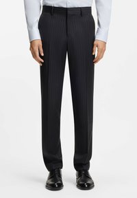 Czarne spodnie w prążki wykonane z gładkiej tkaniny, o prostym kroju, z szlufkami na pasek i przetartym przodem, zestawione z czarnymi skórzanymi butami.