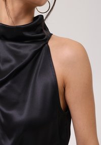 Haut sans manches en satin noir avec un col haut et un design drapé, comportant une épaule dénudée et une texture lisse.