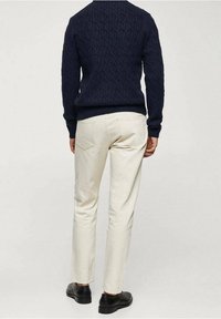 Pull en mailles bleu marine avec un motif texturé, associé à un pantalon slim-fit blanc cassé et des chaussures noires, vu de dos.