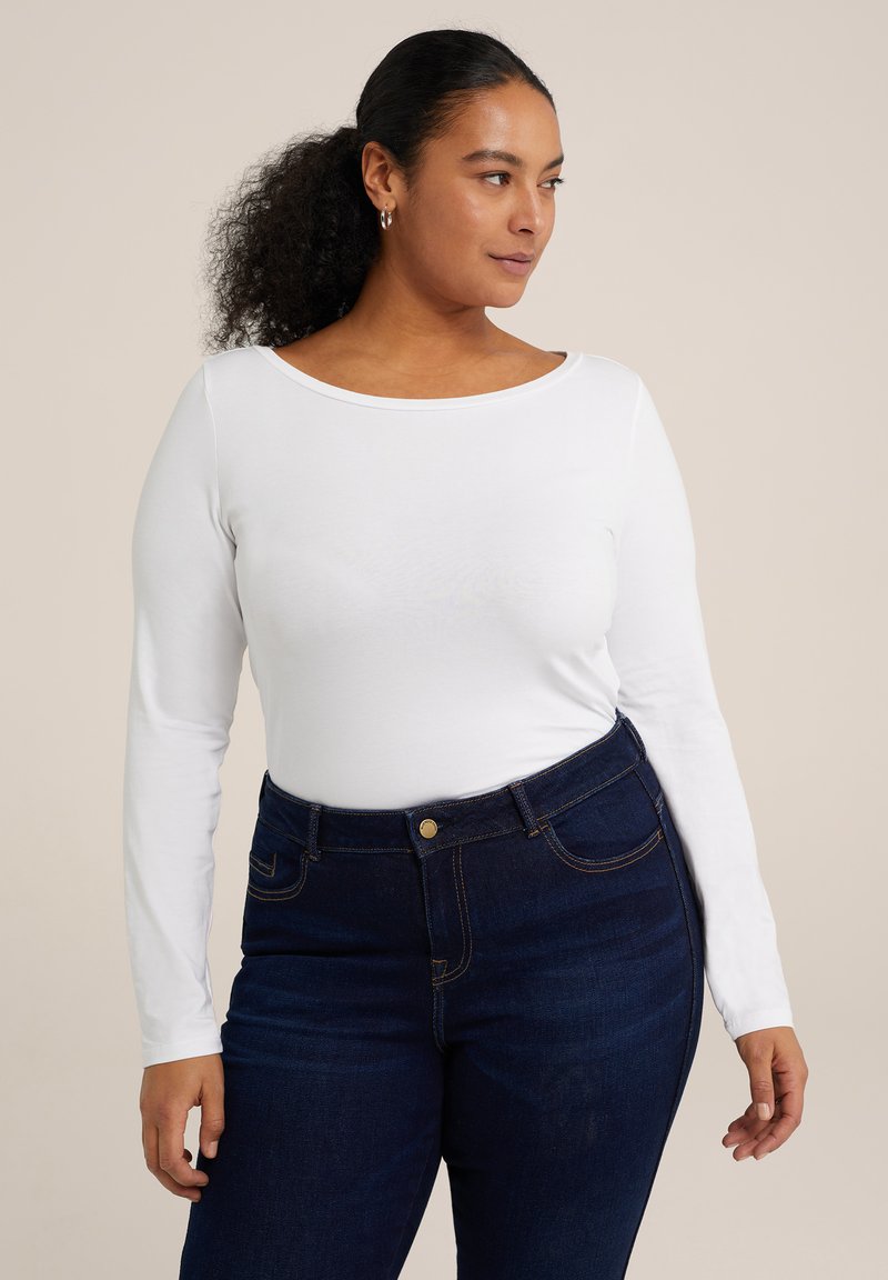 Weißes Langarmoberteil mit weitem Halsausschnitt, kombiniert mit dunkelblauen high-waist Jeans, die mit Steppdetails und Fronttaschen versehen sind.