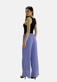 Pantaloni a palazzo viola plissettati con vita elastica, abbinati a un top senza maniche nero. Tessuto liscio, design lungo fino alla caviglia.
