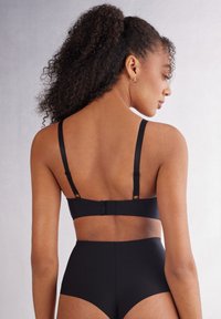 Zwart lingeriesetje met een naadloze bh met verstelbare bandjes en haaksluiting. Hooghangende onderkant met een gladde textuur en een minimalistisch design.