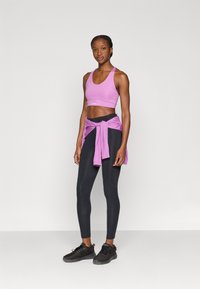 Μωβ αθλητικό σουτιέν, μαύρο κολάν και μαύρα αθλητικά παπούτσια. Το σουτιέν έχει λαιμόκοψη scoop και το πουκάμισο δένεται στη μέση. Ομαλό ύφασμα, εφαρμοστή σχεδίαση.