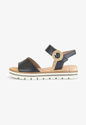 Sandale en cuir noir à bout ouvert, semelle style liège, fond blanc et un accent tressé rond sur la bride.