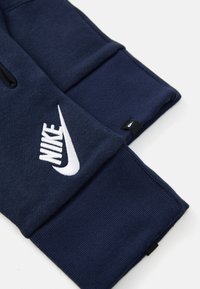 Jūras zila džemperis ar gludu tekstūru, kuram ir liels balts izšūts Nike logo un neliela melna birka iekšpusē piedurknē.
