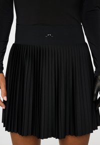 Mustaan pleidatairukku, jossa on leveä vyötärö ja hopeinen yksityiskohta. Kangas näyttää sileältä ja sen rakenne on tasainen koko matkalta.