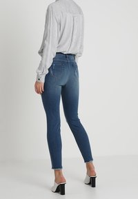 High-waisted, blauwe denim skinny jeans met een vervaagd ontwerp en rafelige zoom; gecombineerd met een lang mouw, verticaal gestreept blouse en mules met blokhak.