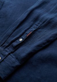Marineblauw linnen shirt met een knoopsluiting en een klein oranje label. Voorzien van een gladde textuur en lange mouwen. Ronde kraag.