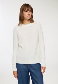 Biały sweter z dzianiny z okrągłym dekoltem, rękawami raglanowymi i ściągaczami, w zestawie z niebieskimi dżinsami. Teksturalny, casualowy fason.