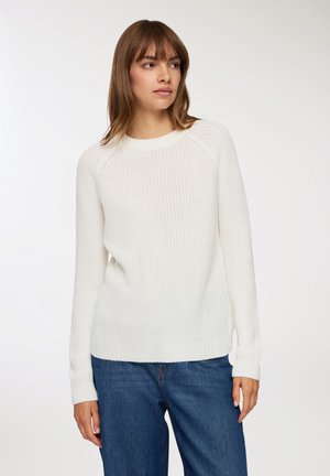 Maglione bianco lavorato a maglia con scollo rotondo, maniche raglan e polsini a costine, abbinato a jeans in denim blu. Design testurizzato e casual.