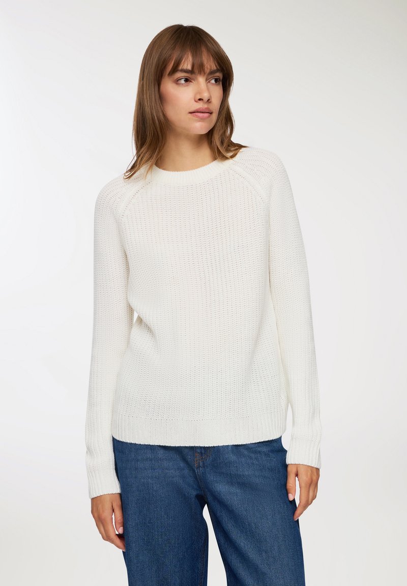 Biały sweter z dzianiny z okrągłym dekoltem, rękawami raglanowymi i ściągaczami, w zestawie z niebieskimi dżinsami. Teksturalny, casualowy fason.