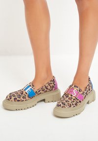 Scarpe slip-on con stampa leopardata e suola chunky beige, dotate di fascette blu e rosa con hardware metallico e tessuto testurizzato.