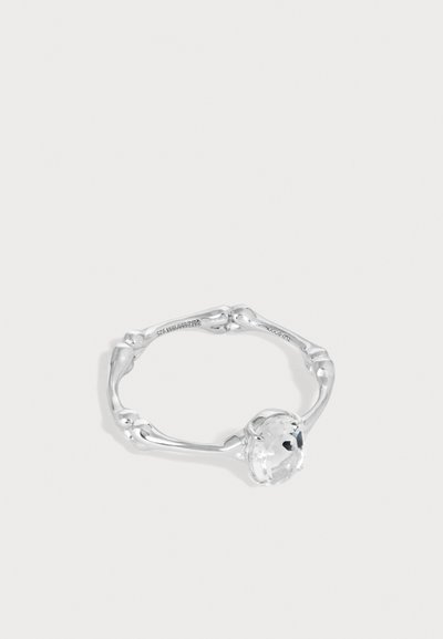 Bague en argent avec une bande torsadée ressemblant à un os, ornée d'une pierre précieuse ronde et claire montée en sertissage à griffes.
