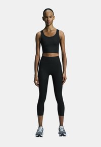 Débardeur noir court et leggings taille haute en matériau lisse et extensible. Logos notables sur le débardeur et les leggings. Chaussures de sport incluses.