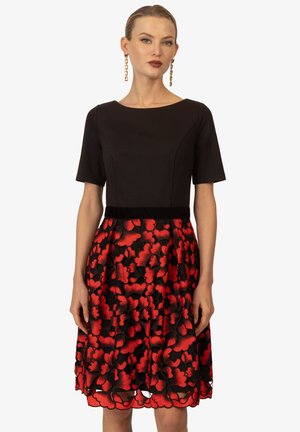 Zwarte jurk met korte mouwen, een getailleerde bodice en een uitlopende rok met een rood bloemenpatroon. Accentueerde tailleband in zwart fluweel.