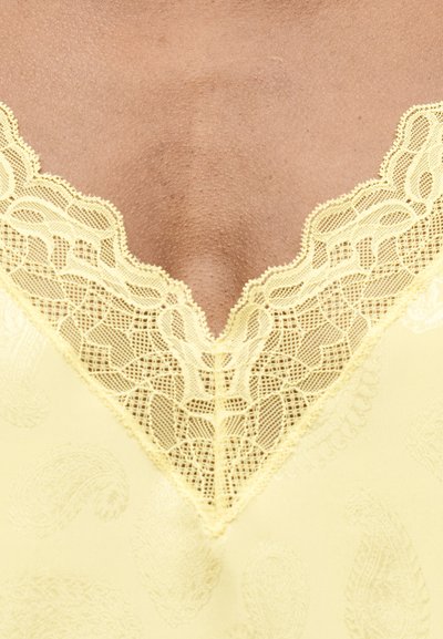 Κοντινό πλάνο δέρματος και κίτρινου υφάσματος με δαντέλα και λεπτό μοτίβο παϊέτας γύρω από ένα V-σχήματος ντεκολτέ.