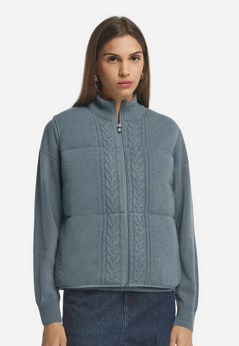 Helles blaues Sweatshirt mit Reißverschluss, Kabelstrickmuster auf der Vorderseite, hohem Kragen und langen Ärmeln, aus weichem Strickstoff gefertigt.