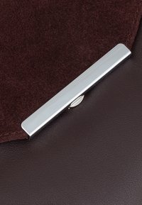 Borsa in pelle marrone con una patta in suede marrone scuro, chiusa con una clasp di metallo argentato. Il contrasto di texture tra la superficie liscia e quella morbida.