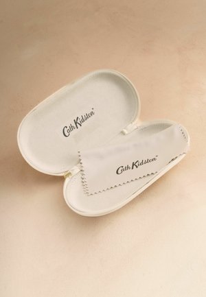 Husă pentru ochelari Cath Kidston de culoare bej deschis, moale, cu o lavetă de curățare asortată și cu marcă, plasată pe o suprafață bej deschis.