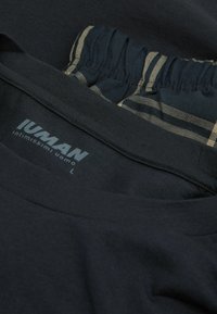 Svart bomullsskjorta med rund halsringning och mjuk textur. Funktioner en etikett med "IUMAN" och en ljusrandig midja invändigt. Storlek L.