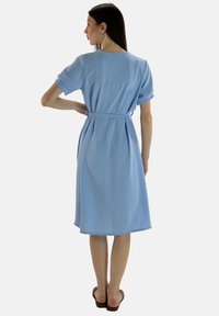 Abito azzurro chiaro a maniche corte con vita aderente, lunghezza al ginocchio, texture liscia e design sobrio e informale, visto da dietro.