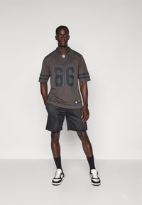 NFL dres u tamno sivoj boji s brojem "66" sprijeda, crne pruge na rukavima. Uparen s crnim mrežastim šortsevima i crno-bijelim tenisicama.