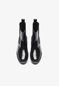 Bottines noires avec une finition en cuir verni brillant, des panneaux latéraux élastiques et des tirants en haut pour un enfilage facile. Design à bout rond.