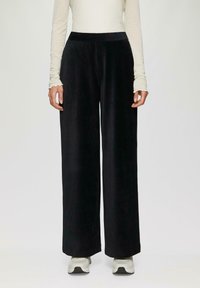 Zwarte fluwelen broek met brede pijpen, een gladde textuur en een elastische tailleband. Gecombineerd met een licht, langmouwtop en sneakers voor een casual uitstraling.